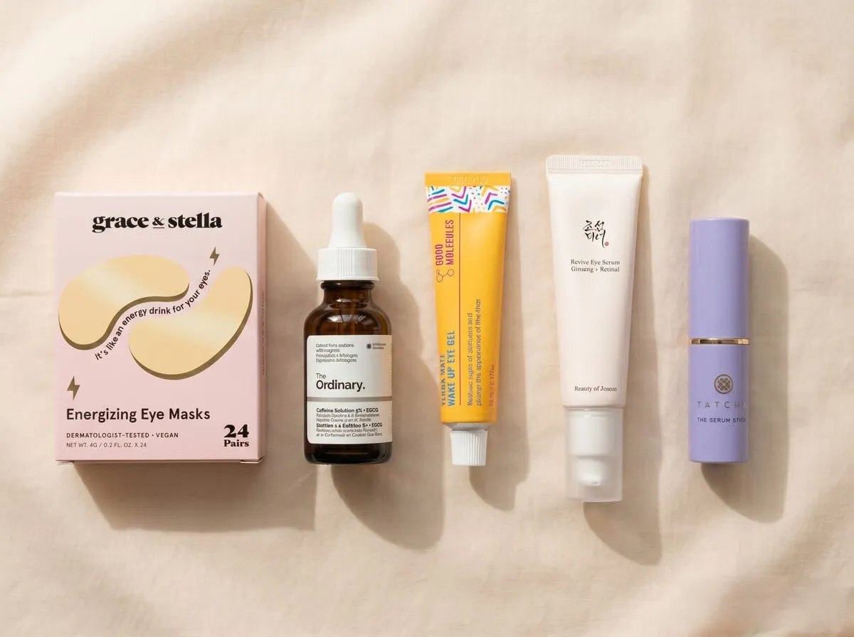 Editorial overhead flat-lay of the five tired-eye rescue picks arranged in a horizontal row on blush linen — grace and stella gold under-eye patches, The Ordinary Caffeine 5% + EGCG glass dropper bottle, Good Molecules Yerba Mate Wake Up Eye Gel tube, Beauty of Joseon Revive Eye Serum pink tube with silver pump base, and Tatcha The Serum Stick twist-up tube