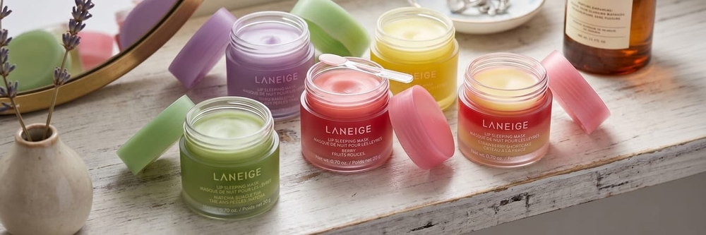 Five LANEIGE Lip Sleeping Mask flavors lined up open on a styled shelf, with the Berry jar and its spatula in the center