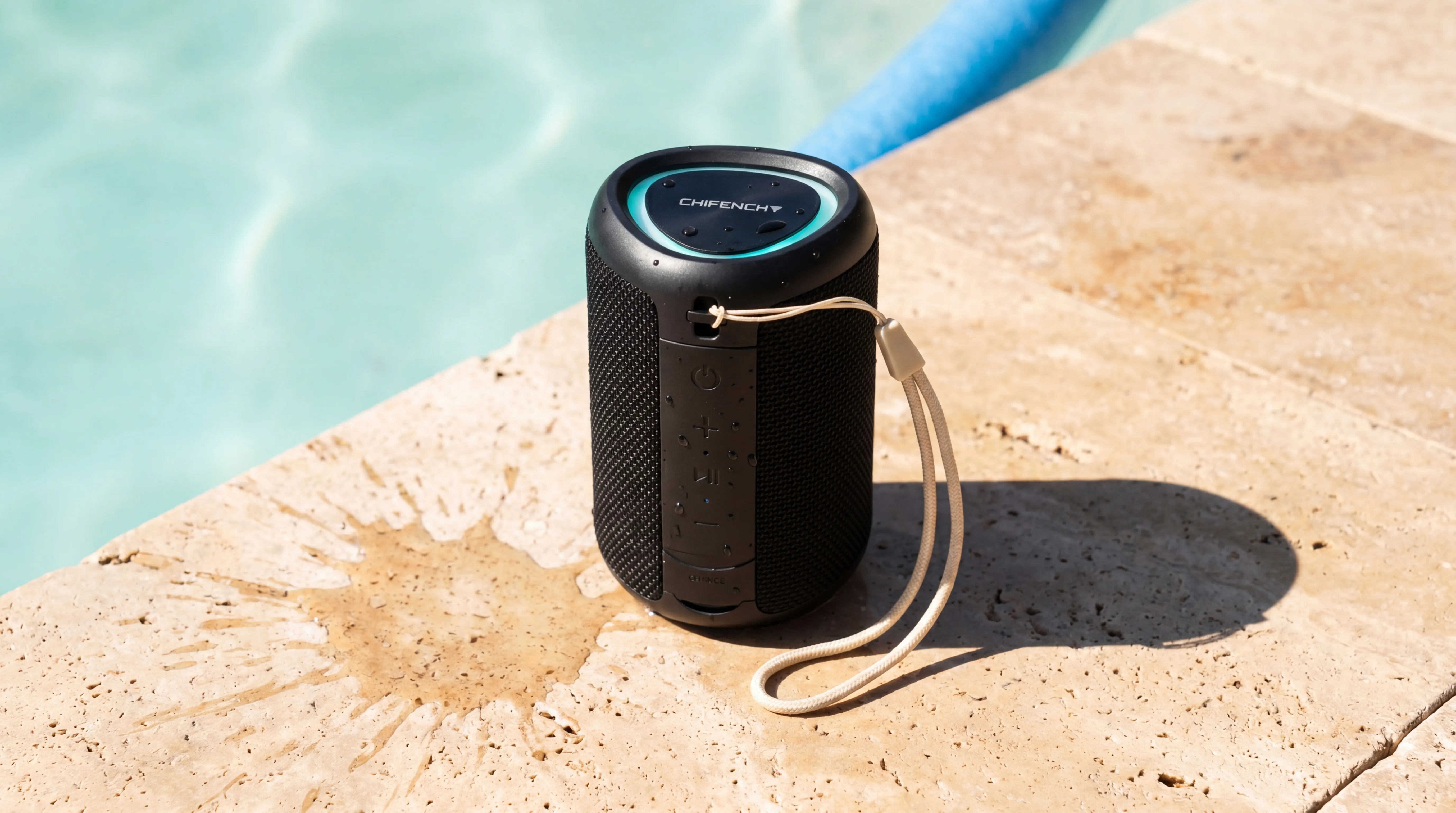 CHIFENCHY speaker on a beach towel beside sunscreen and sunglasses, ocean in soft focus